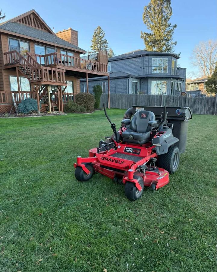 Red zero-turn mower parked on a fresh cut lawn in front of a house with a two-storey deck at dusk