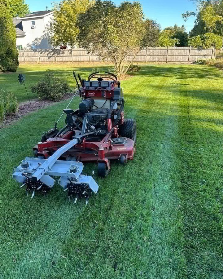 Red stand-on aerator parked on a striped lawn in front of a wooden fence