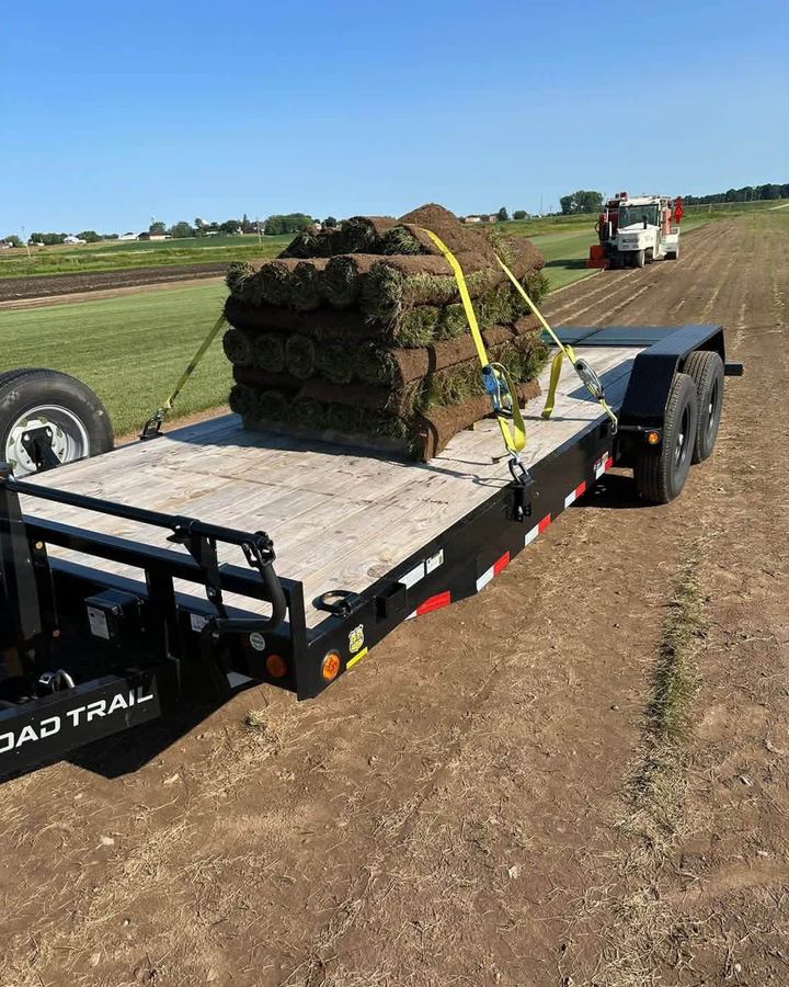 Pallet of rolled sod strapped to a flatbed trailer parked on bare prepared ground